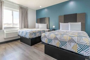 A hotel room with two beds, a window with curtains, a wall-mounted air conditioner, and a blue accent wall.