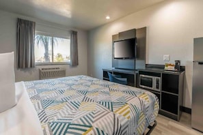A hotel room with a bed, a desk with a computer, a television, and a refrigerator.