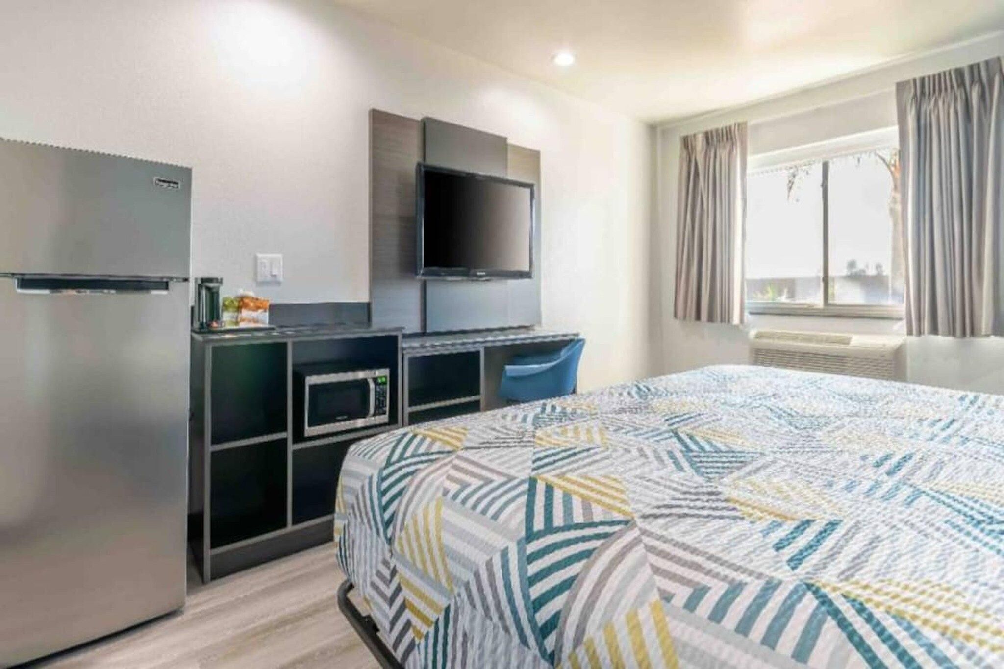 Ein Hotelzimmer mit einem Bett, einem Flachbildfernseher, einer Mikrowelle und einem Kühlschrank.