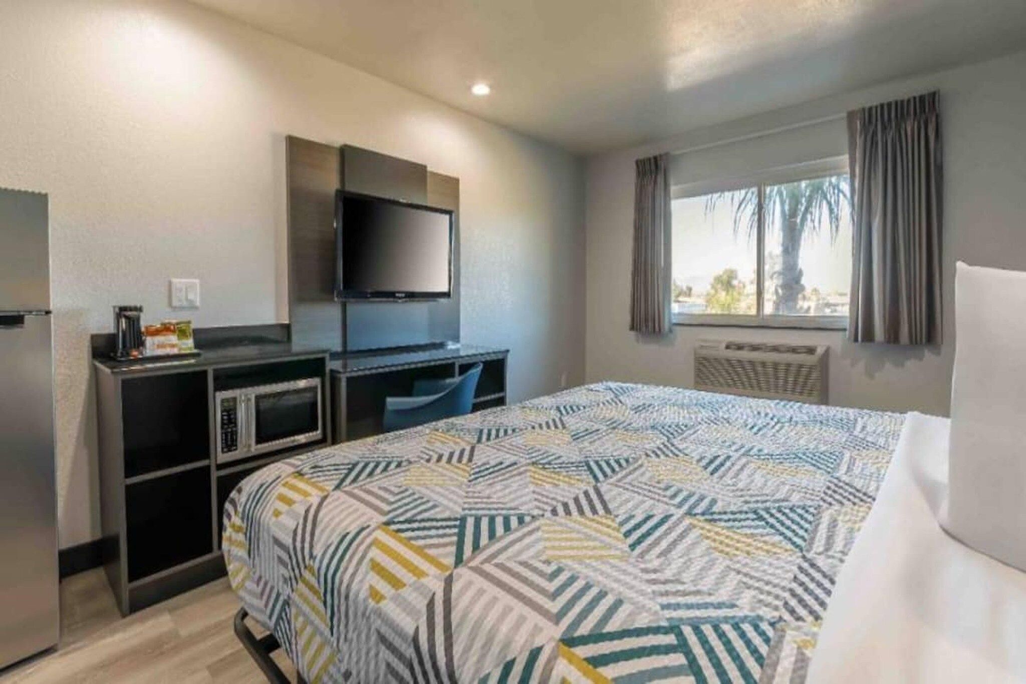 A hotel room with a bed, a desk with a computer, a television, and a window with curtains.