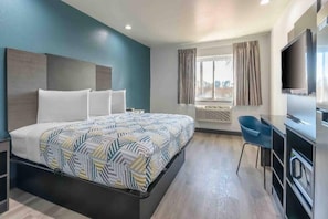 Una habitación de hotel con una cama, un escritorio, una silla, un televisor y una ventana con cortinas.