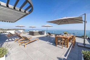 Een dakterras met lounge fauteuils, parasols, een jacuzzi en een eettafel gedekt voor twee personen.