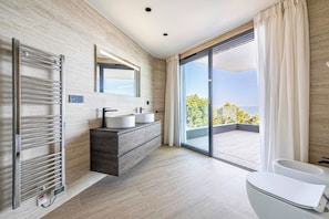 Een moderne badkamer met een ingebouwd toilet, een wastafel met spiegel en een groot raam met uitzicht op bomen.
