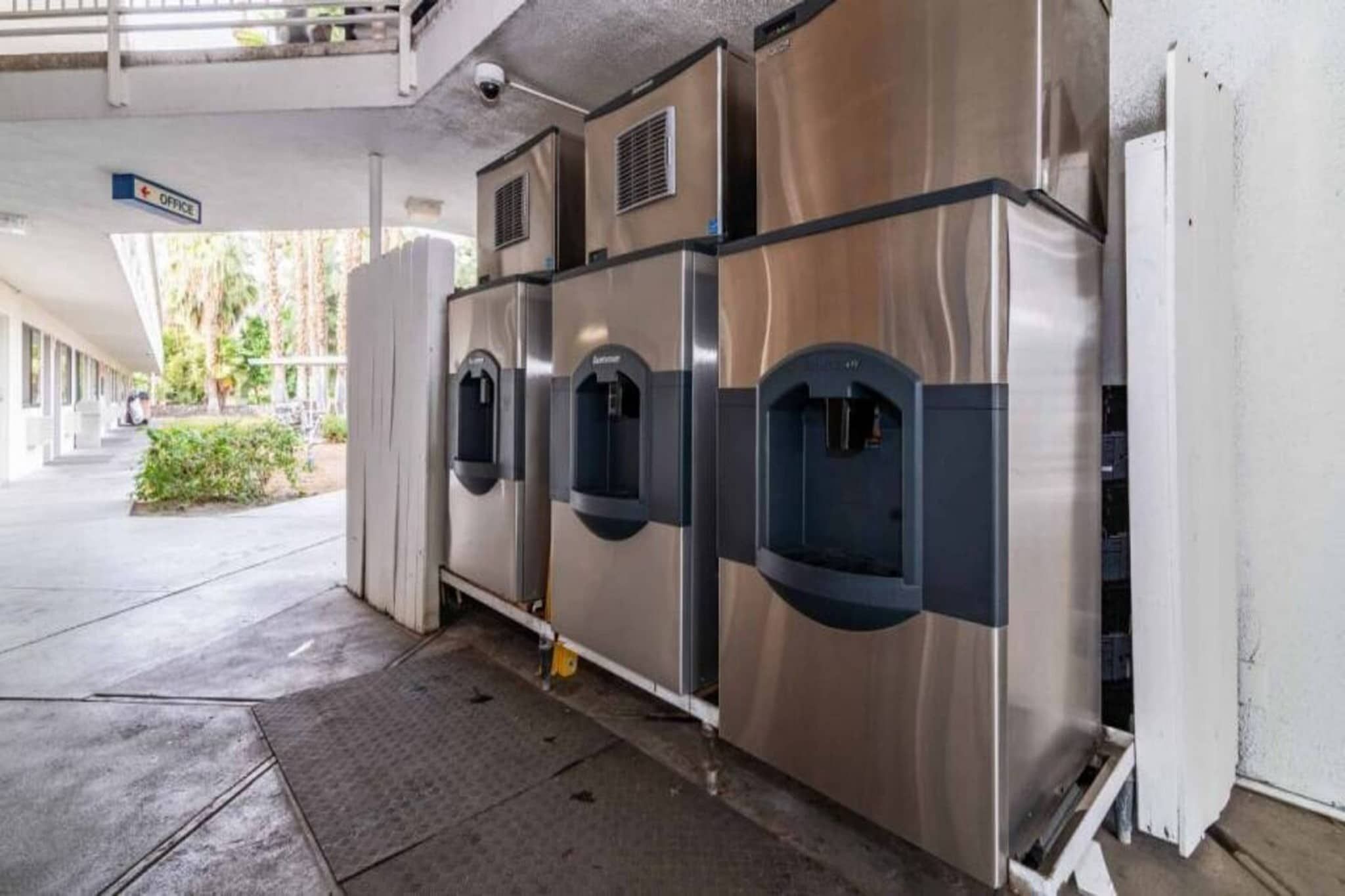 A row of stainless steel self-service beverage dispensers in a covered outdoor area.