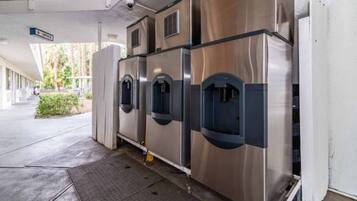 A row of stainless steel self-service beverage dispensers in a covered outdoor area.