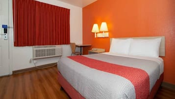 A hotel room with a bed, a desk, a chair, a telephone, and a window with red curtains.