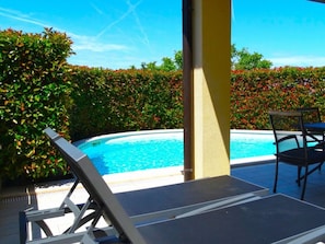 Ein Poolbereich mit Liegestuhl, Tisch und Blick auf einen von Grünflächen umgebenen Pool.