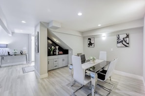 Une cuisine moderne avec des meubles blancs, un plan de travail noir et un coin repas comprenant une table en verre et des chaises blanches.