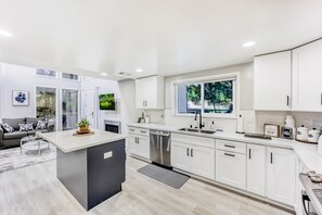 Une cuisine moderne avec des meubles blancs, un îlot central et une grande fenêtre.