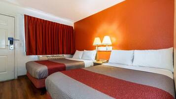 Quarto de hotel com duas camas, uma cortina vermelha, uma luminária fixada na parede e uma porta com tranca.