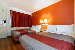 Quarto de hotel com duas camas, uma cortina vermelha, uma luminária fixada na parede e uma porta com tranca.