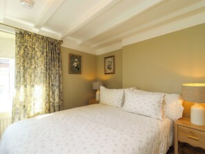 A bedroom with a bed, two bedside tables, a lamp, and floral-patterned curtains. - Blueberry Cottage (Malton)