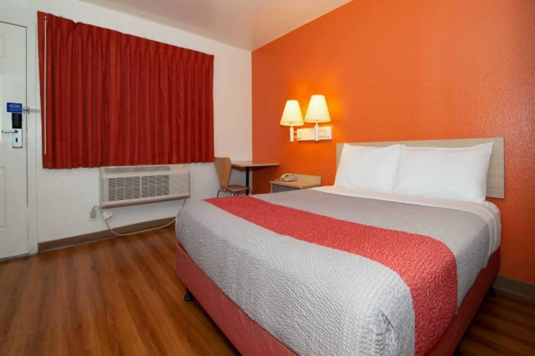 Een hotelkamer met een bed, bureau, stoel, telefoon en een raam met rode gordijnen.