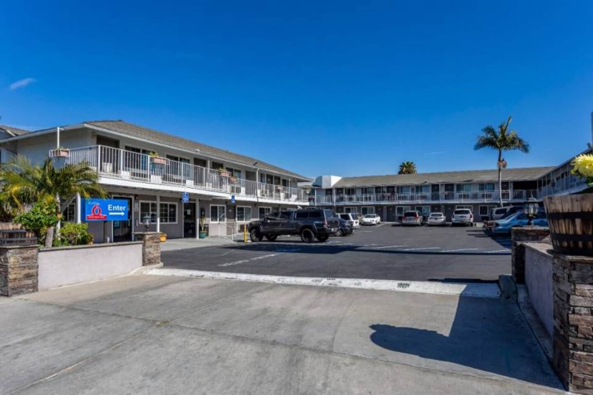 Ein Motel mit Parkplatz, mehreren Fahrzeugen und blauem Himmel.