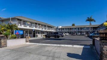 Ein Motel mit Parkplatz, mehreren Fahrzeugen und blauem Himmel.