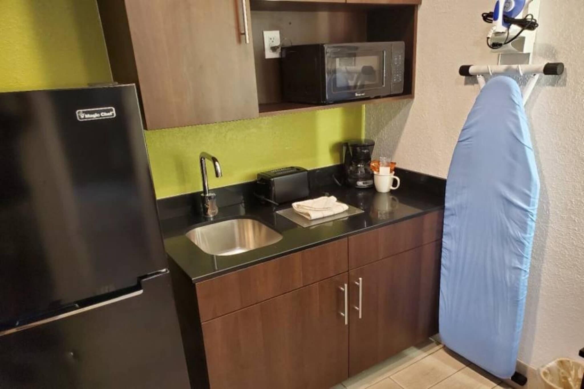 Una cocina compacta equipada con refrigerador, microondas, lavamanos y cafetera.
