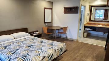 Habitación de hotel con cama, escritorio, silla, espejo y baño con lavamanos e inodoro.