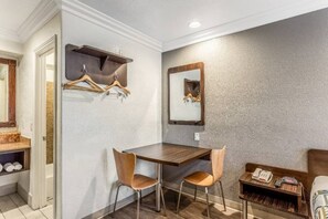 Een hotelkamer met een houten eettafel, twee stoelen, een spiegel en een plank met kledinghangers.