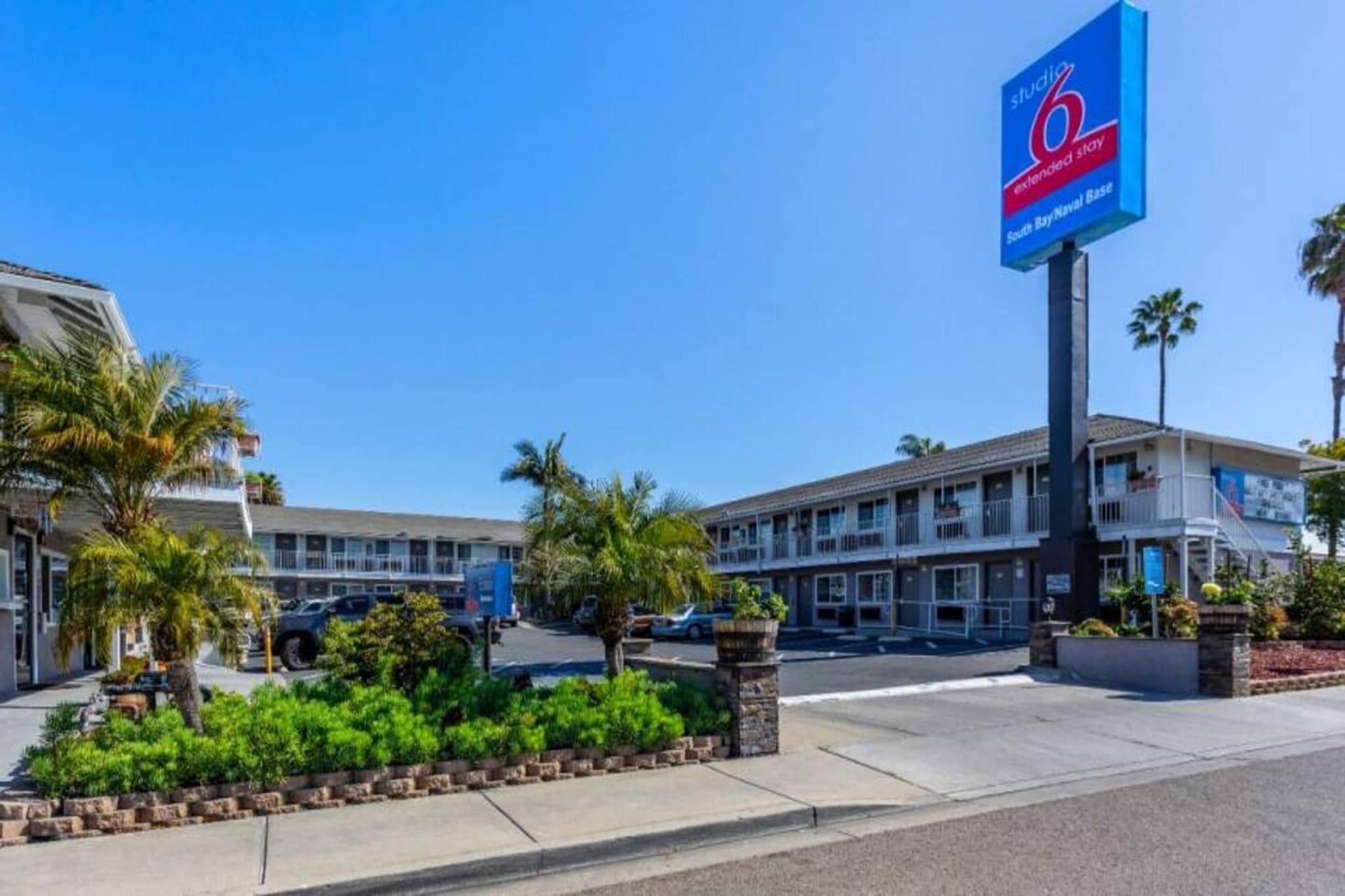 Un hotel con un gran letrero azul, varios pisos y un estacionamiento.