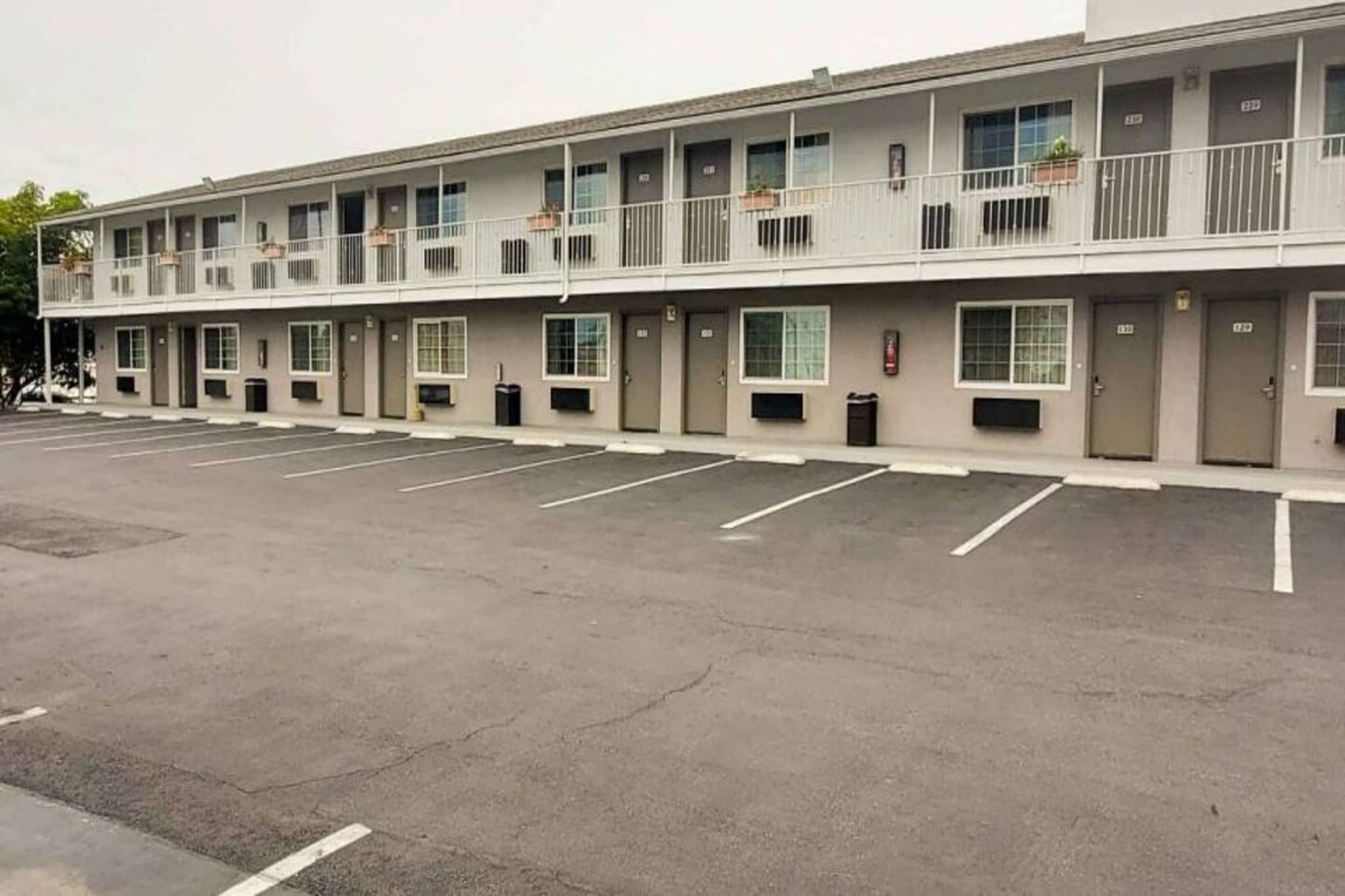 Ein mehrstöckiges Motel mit einer Reihe von Zimmern, einem Parkplatz und einem Hydranten.