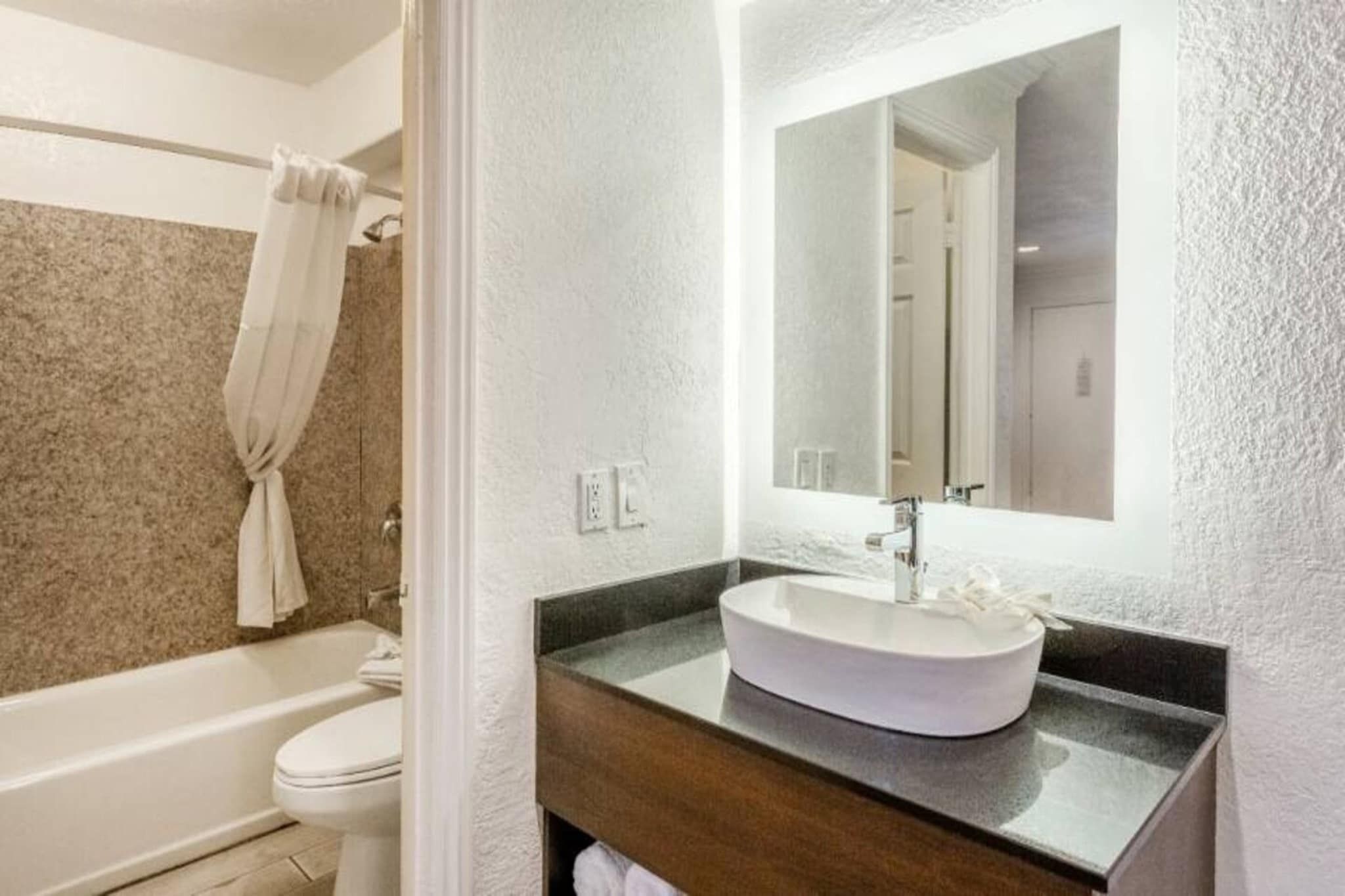 Un baño moderno con una bañera independiente, un lavabo blanco con un espejo grande arriba y una toalla colgada en la pared.