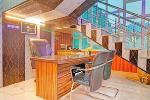 A reception desk with a computer, a telephone, and a chair. There is a staircase with glass railings and a view of the outside. - Townhouse Railway Road Srinagar  (Srinagar)