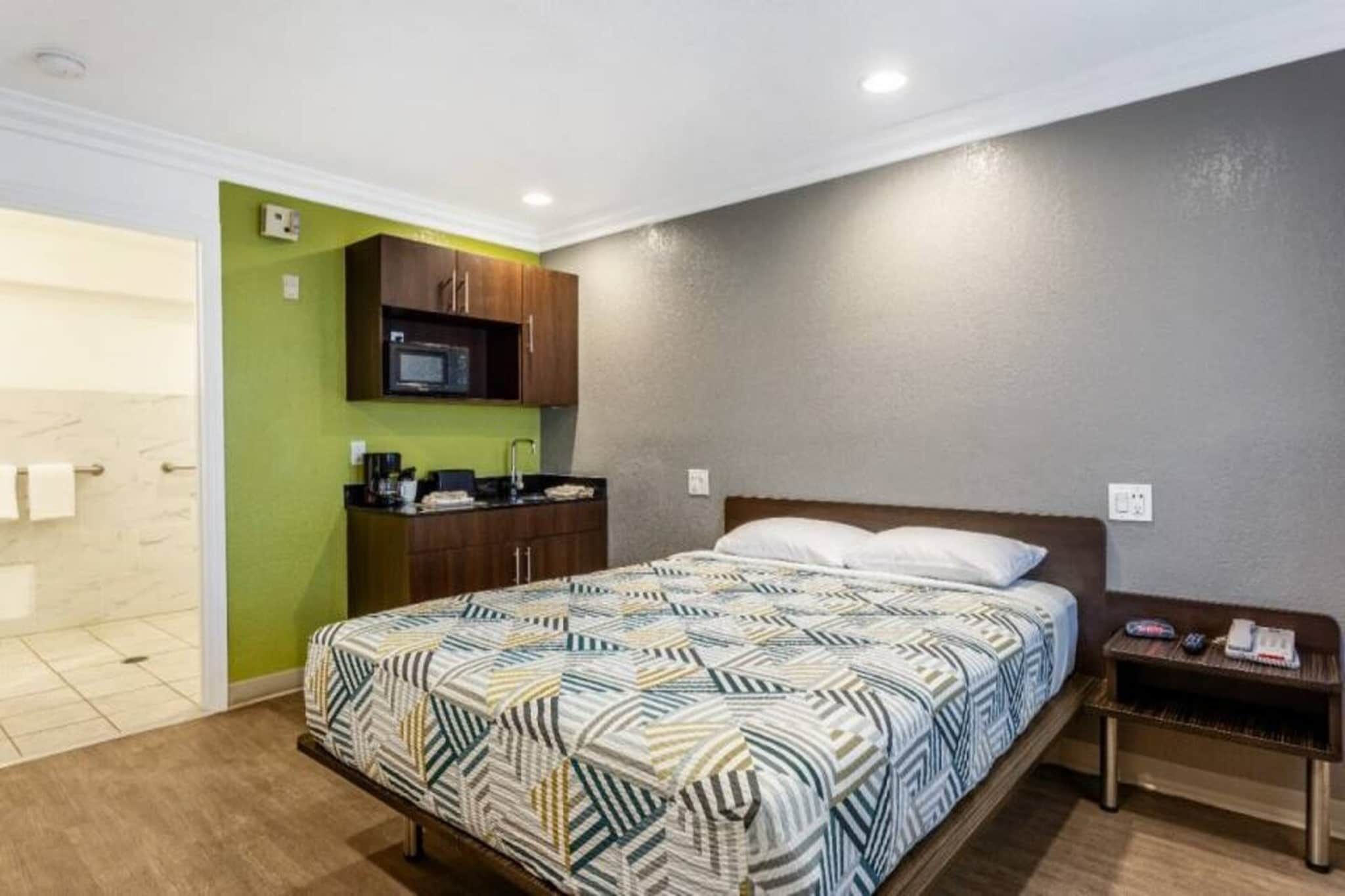 A hotel room with a bed, a small bedside table, a microwave, and a green wall.