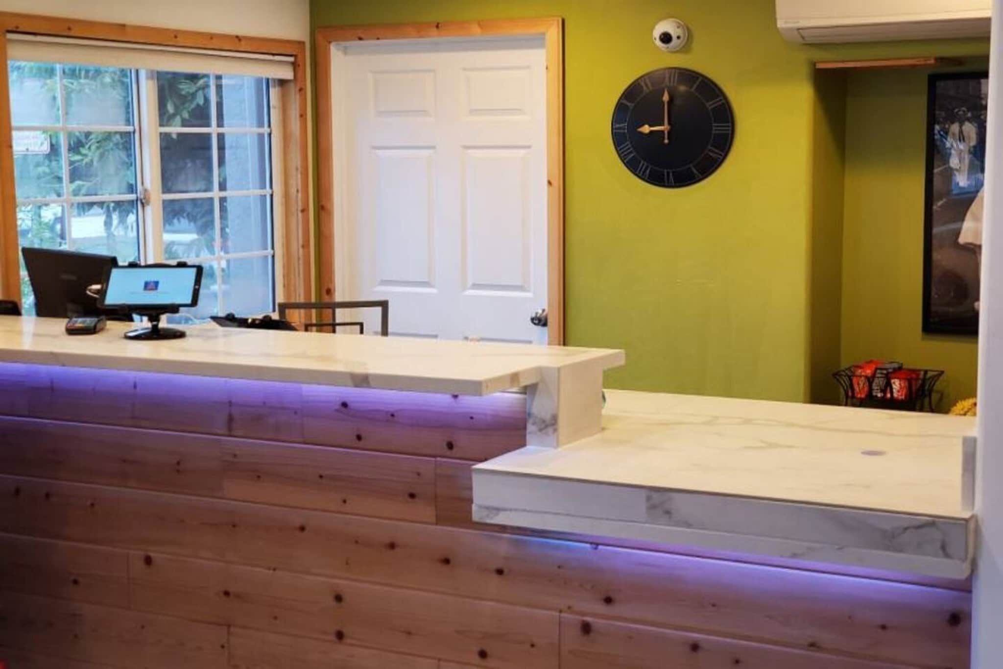 Un comptoir d’accueil avec un ordinateur, une horloge et une porte, dans une pièce aux murs verts.