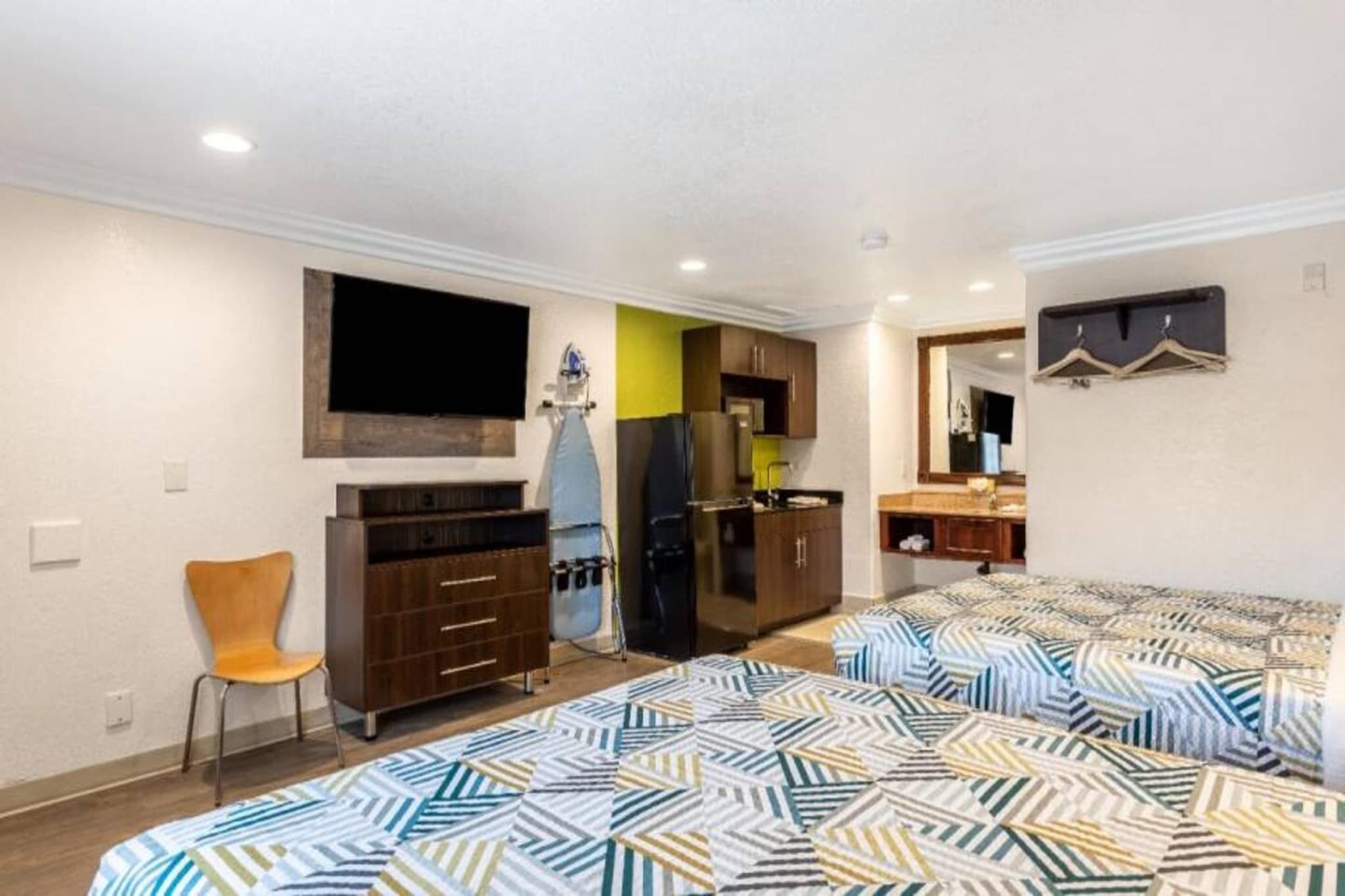 A compact room with a bed, a chair, a TV, a kitchenette, and a bathroom.