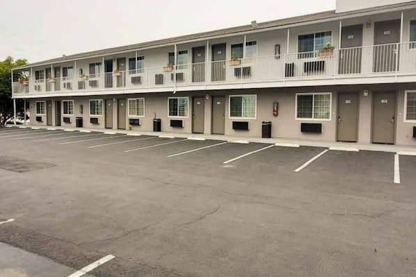 Een meerhoog motel met een rij kamers, een parkeerplaats en een brandkraan.