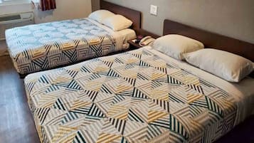 Two double beds with patterned bedding in a room with a window and a wall socket.