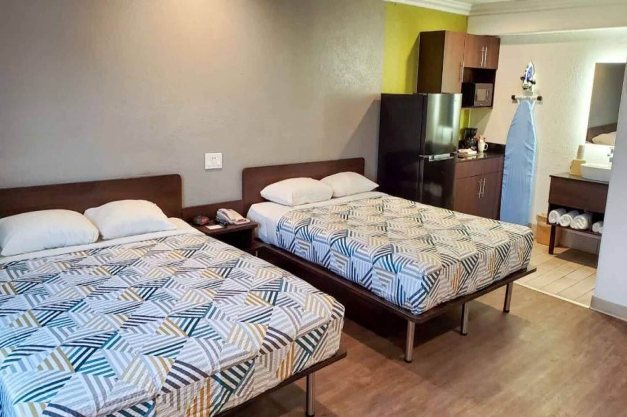 A hotel room with two beds, a kitchenette, and a bathroom.