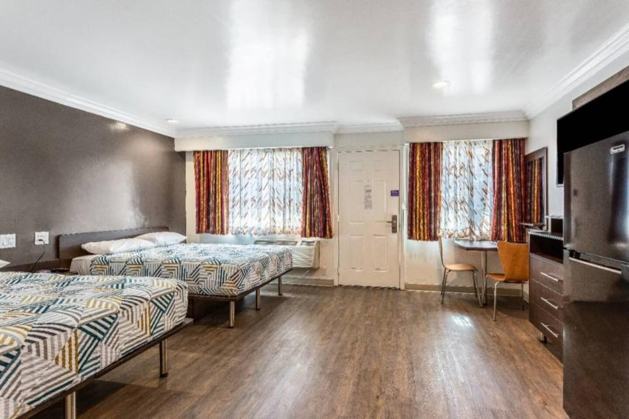 Une chambre d’hôtel avec trois lits, un bureau, une chaise et un téléviseur.