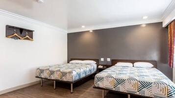 A hotel room with two single beds, a small bedside table, a wall-mounted coat rack, and a plain wall.