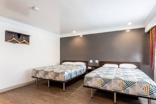A hotel room with two single beds, a small bedside table, a wall-mounted coat rack, and a plain wall.