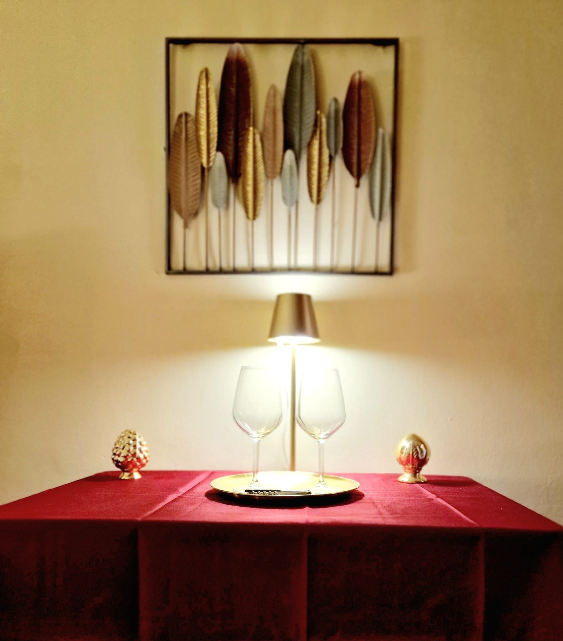 Ein Tisch mit rotem Tischtuch, zwei Weingläsern und einer Lampe.