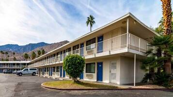 A motel with a two-story structure, a parking lot, and a mountainous backdrop.