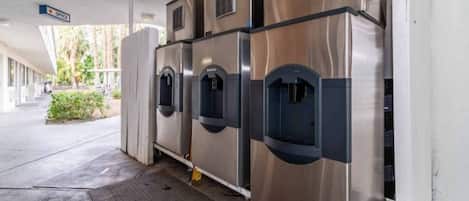 Una hilera de dispensadores automáticos de bebidas de acero inoxidable en un área exterior techada.