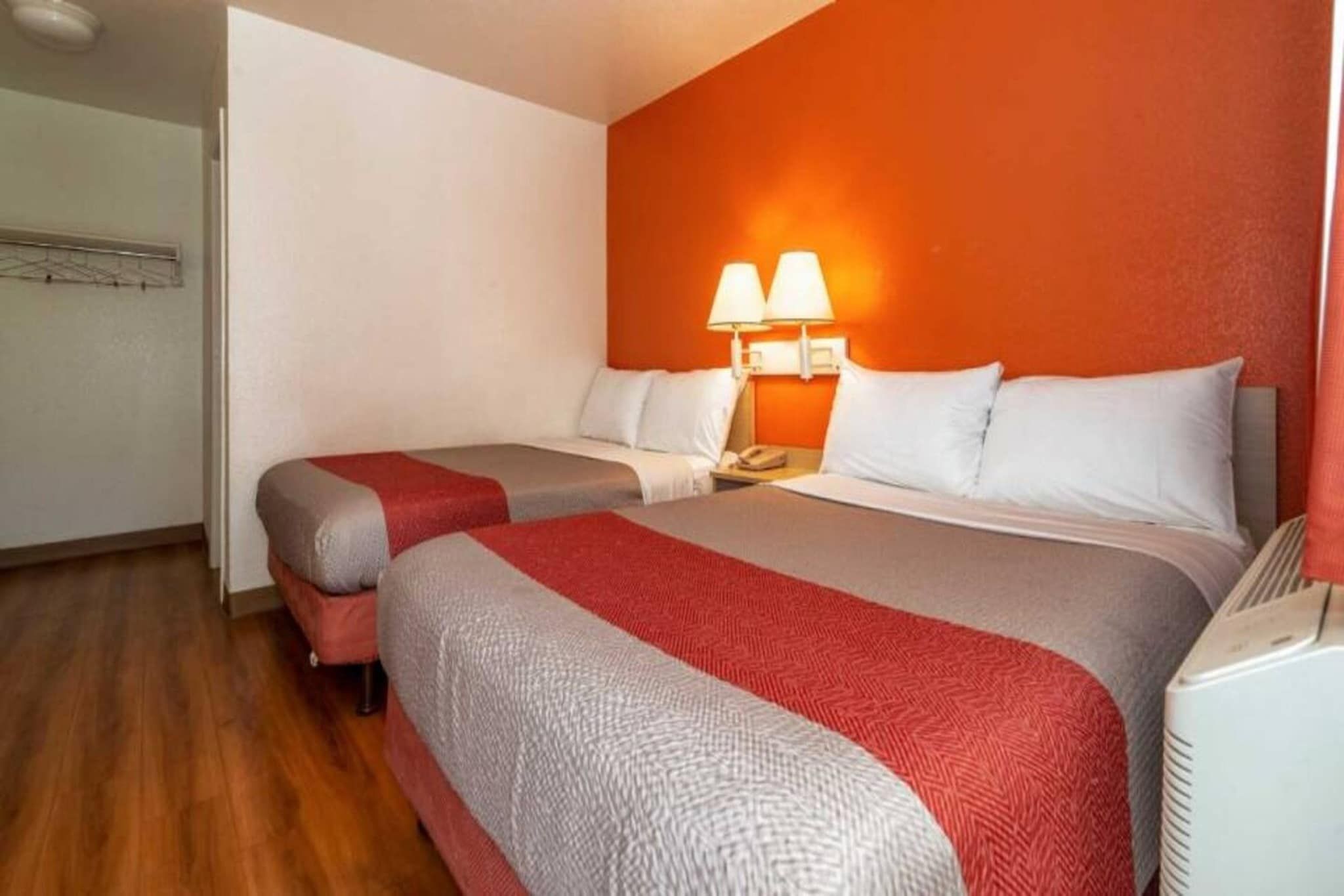 Quarto de hotel com duas camas, uma mesinha de cabeceira e um aquecedor fixado na parede.