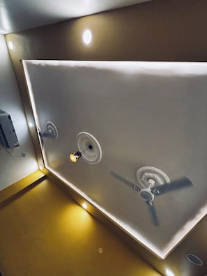 A modern bathroom with a large mirror, a ceiling fan, and recessed lighting. - Shree Shubhgiri Inn (Ayodhya)