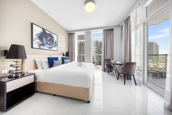 Quarto de hotel com cama, mesa de cabeceira, luminária, obra de arte e varanda com mesa e cadeira.