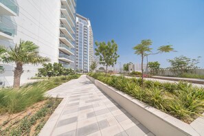 A modern residential building with a paved walkway, greenery, and a clear sky. - StayShort - Cozy Studio in Damac Hills 1 for 2 with Pool Access! (Damac HIlls 1)
