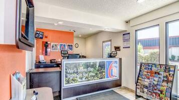 A reception desk with a digital screen, a clock, and a window with a view of the outside.