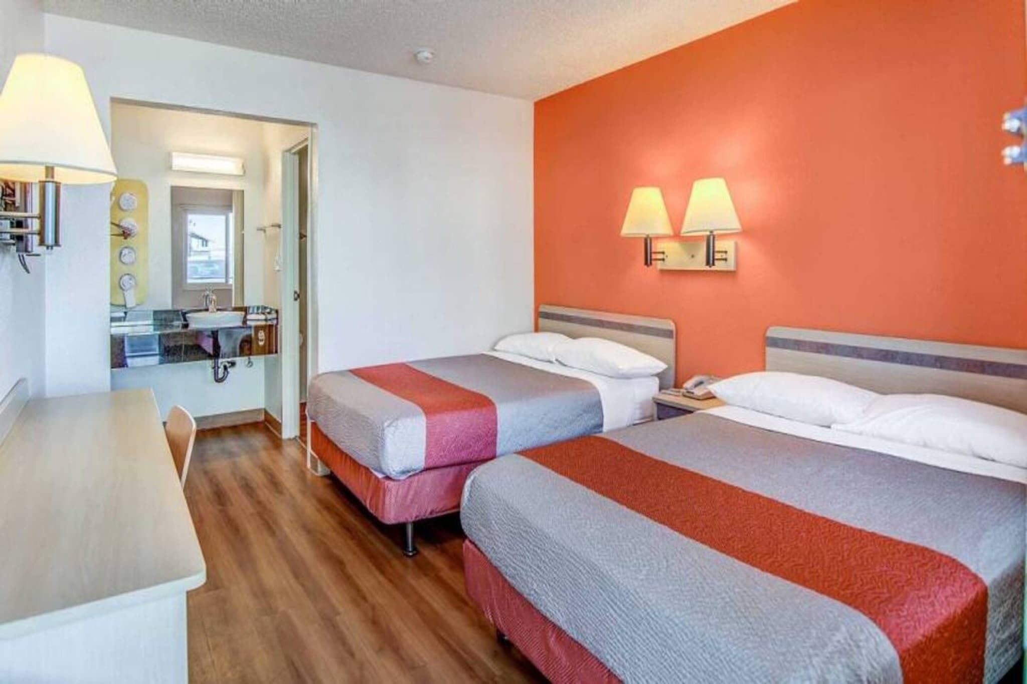Ein Hotelzimmer mit zwei Betten, einem Schreibtisch und einem durch eine geöffnete Tür sichtbaren Badezimmer.