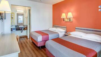 Ein Hotelzimmer mit zwei Betten, einem Schreibtisch und einem durch eine geöffnete Tür sichtbaren Badezimmer.
