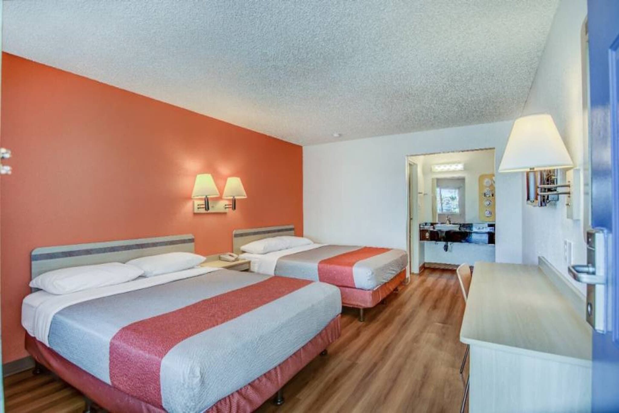 A hotel room with two beds, a desk, a mirror, and a bathroom visible through an open door.