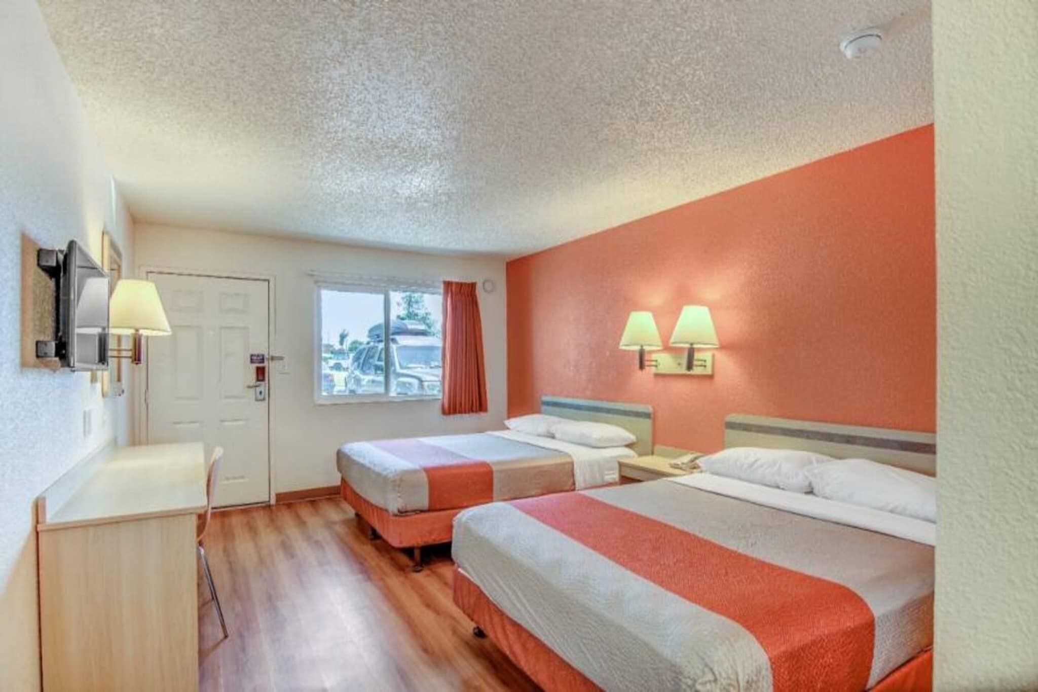 A hotel room with two beds, a desk, and a window.