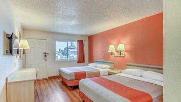 A hotel room with two beds, a desk, and a window.
