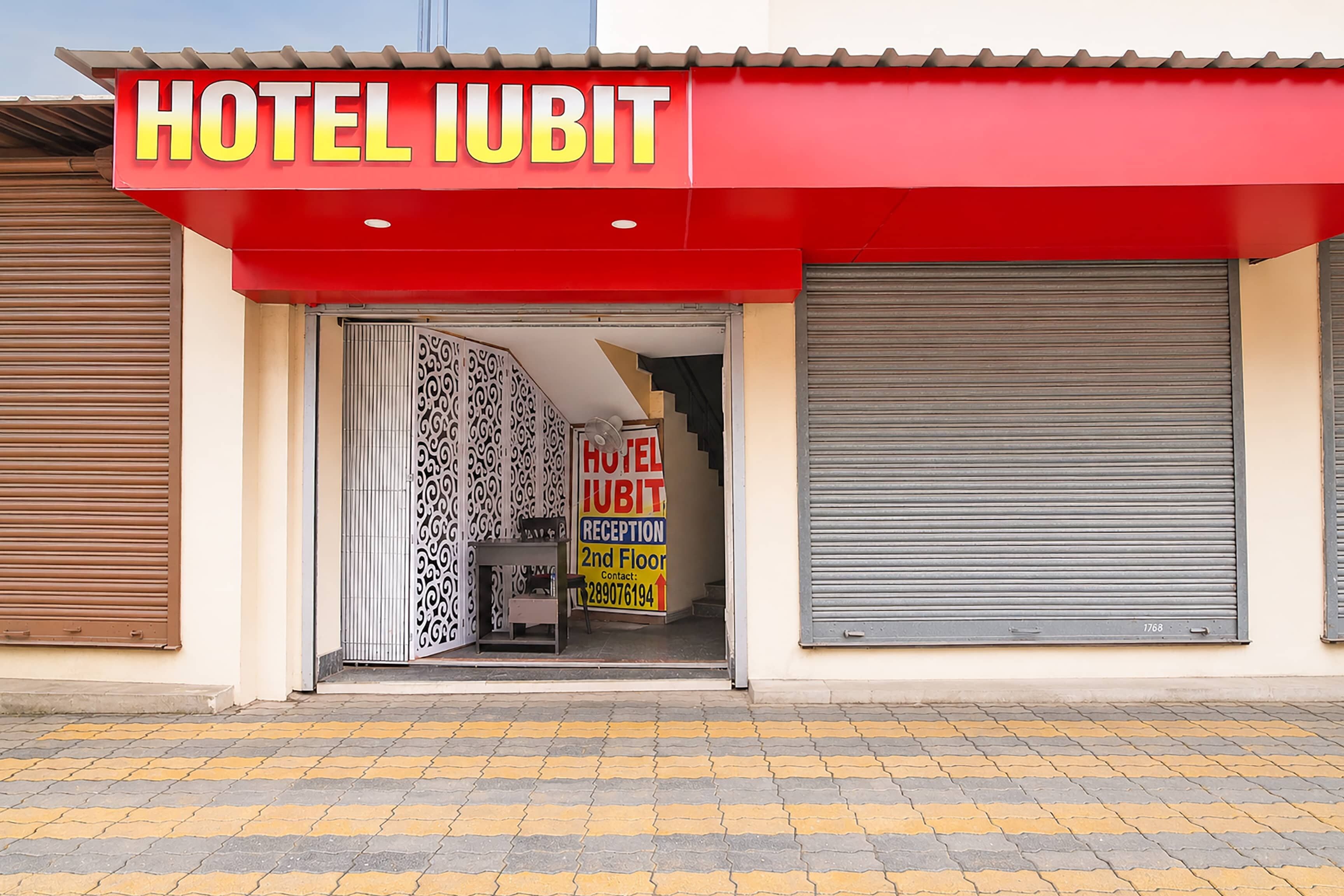 Hotellin sisäänkäynti, jonka yläpuolella on punainen markiisi, jossa lukee »HOTEL IUBIT», ja sen sisällä vastaanottotiski.