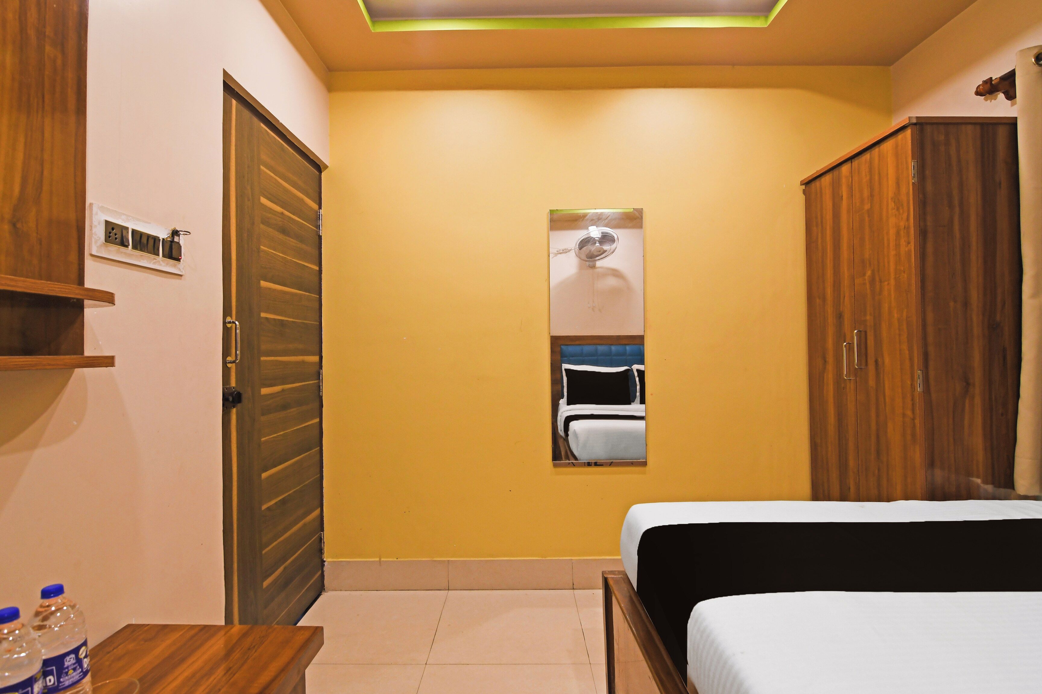 A bedroom with a bed, a wardrobe, a mirror, and a small table with water bottles.